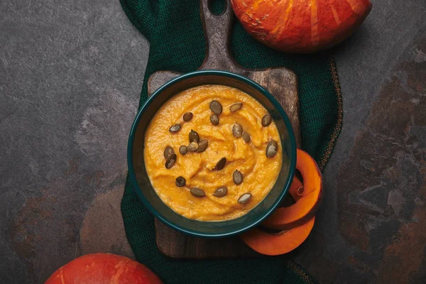 Vista superior de la sopa de calabaza saludable en tazón y calabazas frescas en la superficie oscura - foto de stock