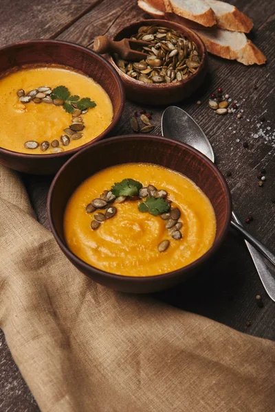 Deliziosa zuppa di zucca in ciotole con cucchiai e sacco sul tavolo di legno — Foto stock