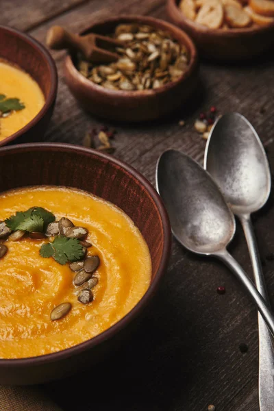 Vista ravvicinata di deliziosa zuppa di zucca in ciotole e cucchiai su tavolo di legno — Foto stock