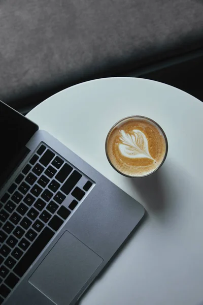 Top view of cup of cappuccino and laptop on table in cafe — Stock Photo