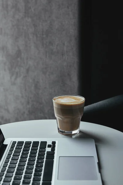 Primo piano vista del computer portatile e tazza di cappuccino sul tavolo nel caffè — Foto stock