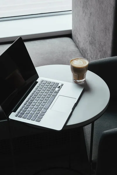 Laptop com tela em branco na mesa e xícara de cappuccino no café — Fotografia de Stock