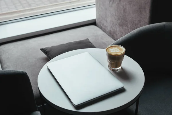 Vista de ángulo alto de la computadora portátil y la taza de capuchino en la mesa en la cafetería - foto de stock