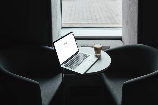 Laptop mit google-Webseite und Tasse Kaffee auf dem Tisch im Café — Stockfoto