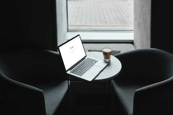 Laptop with google website and cup of coffee on table in cafe — Stock Photo