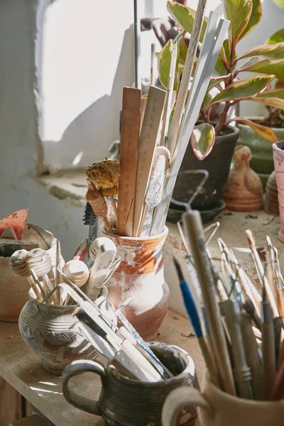 Selective focus of pottery tools and paintbrushes at table in pottery studio — Stock Photo