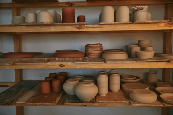 Cuencos de cerámica y platos en estantes de madera en el estudio de cerámica - foto de stock