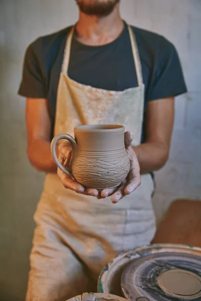 Image recadrée de potier dans tablier tenant pot d'argile à l'atelier — Photo de stock