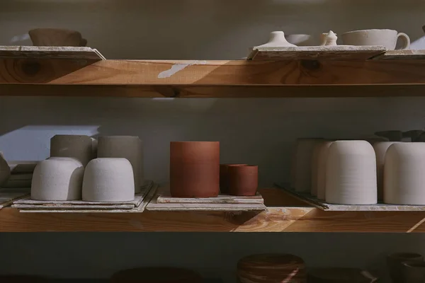 Ceramic bowls and dishes on wooden shelves at pottery studio — Stock Photo