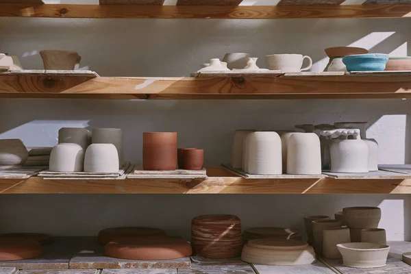 Ceramic bowls and dishes on wooden shelves at pottery studio — Stock Photo