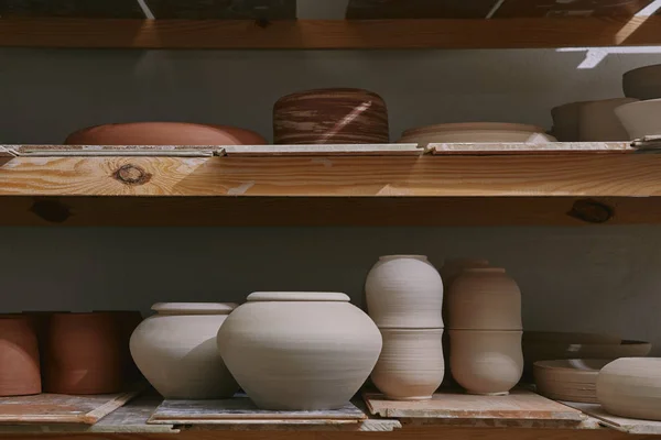 Cuencos de cerámica y platos en estantes de madera en el estudio de cerámica — Stock Photo