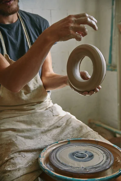 Vue partielle du potier professionnel dans le tablier tenant l'argile au studio de poterie — Photo de stock