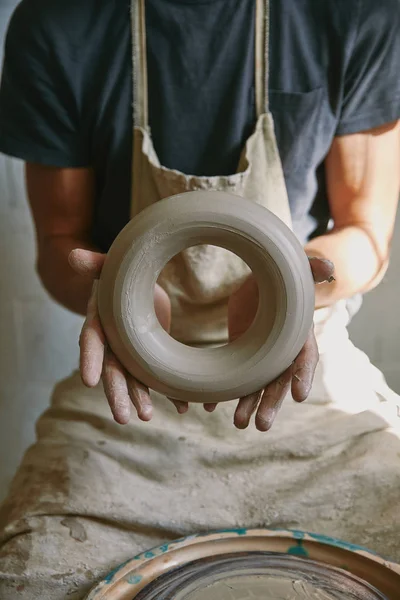 Imagen recortada de alfarero profesional en delantal que sostiene la arcilla en el estudio de cerámica — Stock Photo