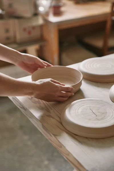 Imagen recortada de la mujer poniendo plato de cerámica en la mesa en el taller - foto de stock