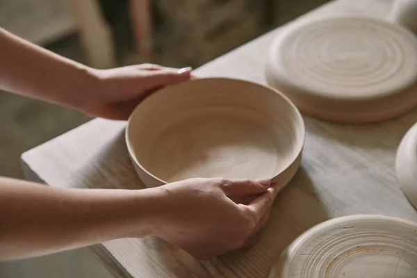 Vista parcial de la mujer poniendo plato de cerámica en la mesa en el taller - foto de stock