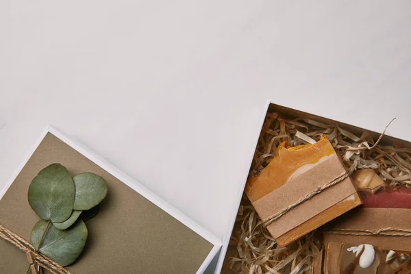 Vista dall'alto della confezione regalo decorata con foglie di eucalipto con sapone all'interno su superficie in marmo bianco — Foto stock