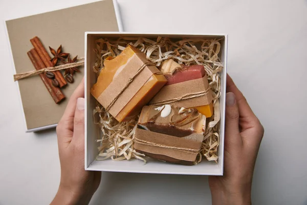 Plan recadré de femme tenant boîte de savon fait à la main sur la surface de marbre blanc — Photo de stock