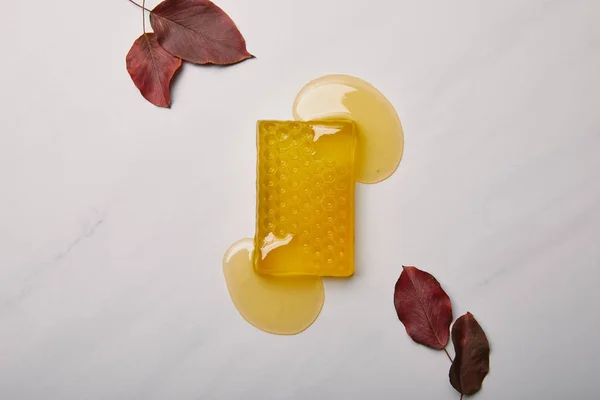 Vista superior de sabão artesanal em forma de favo de mel com folhas vermelhas na superfície de mármore branco — Fotografia de Stock