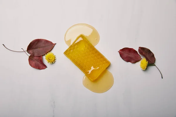 Vue du dessus du savon au miel avec des pissenlits et des feuilles sur une surface en marbre blanc — Photo de stock