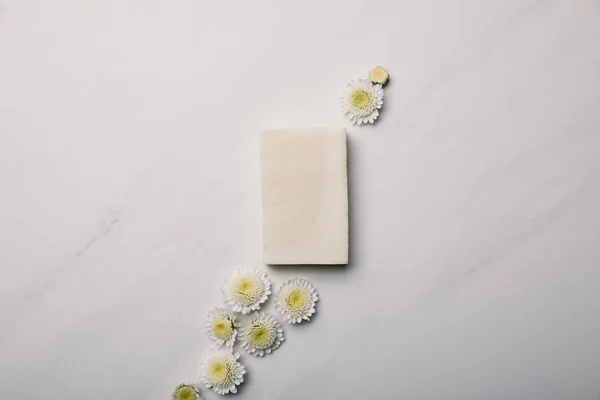 Vue de dessus du morceau de savon blanc avec des marguerites sur la surface de marbre blanc — Photo de stock