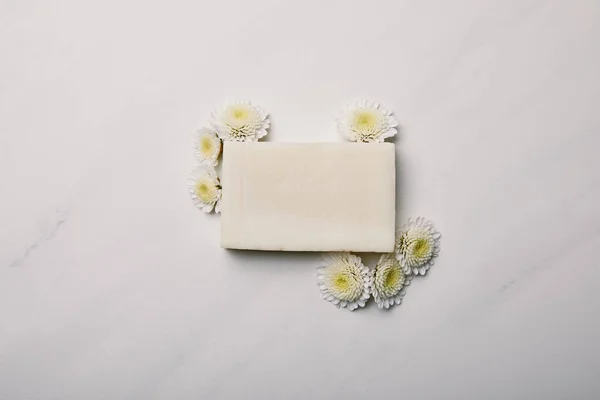 Vue de dessus du morceau de savon fait à la main avec des marguerites sur la surface de marbre blanc — Photo de stock