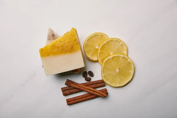Vista dall'alto del sapone fatto a mano con fette di limone, cannella e caffè sulla superficie di marmo bianco — Foto stock