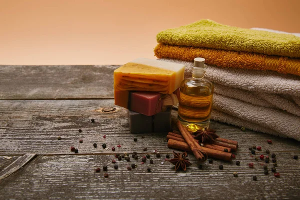 Close-up de peças de sabão aromático artesanal com toalhas empilhadas, especiarias e óleo de massagem em mesa de madeira rústica — Fotografia de Stock