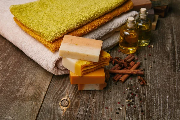 Primer plano de piezas de jabón hechas a mano con toallas apiladas, especias y aceite de masaje en la mesa de madera rústica - foto de stock