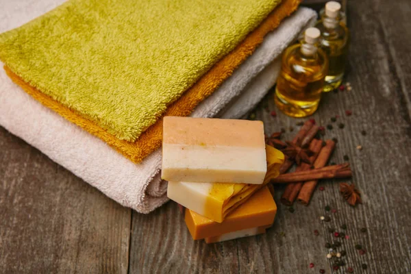 Primer plano de piezas de jabón con toallas apiladas, especias y aceite de masaje en la mesa de madera rústica - foto de stock