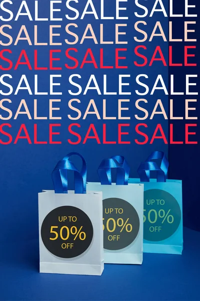 Close up view of paper shopping bags arranged on blue backdrop sale signs and 50 percents discount — Stock Photo