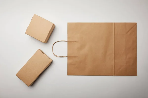 Vista superior de la bolsa de papel de entrega de alimentos y cajas de cartón en la superficie blanca - foto de stock