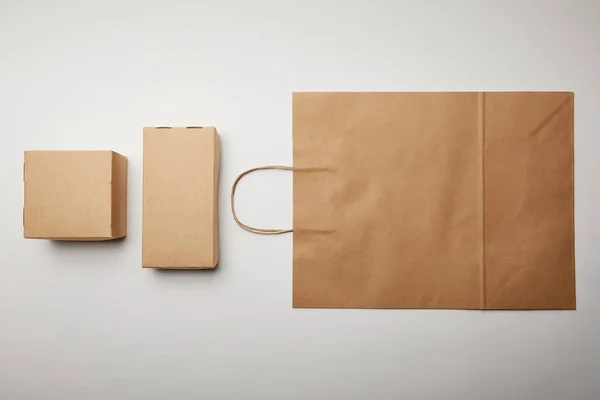 Vista elevada de vista arreglada de cajas de cartón y bolsa de papel de entrega de alimentos en la superficie blanca, concepto minimalista - foto de stock