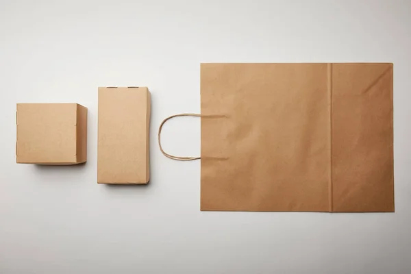 Elevated view of arranged view of cardboard boxes and food delivery paper bag on white surface, minimalistic concept — Stock Photo