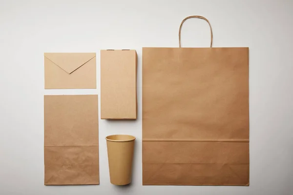 Flay lay con busta, bicchiere di carta, sacchetto di carta consegna cibo su superficie bianca, concetto minimalista — Foto stock