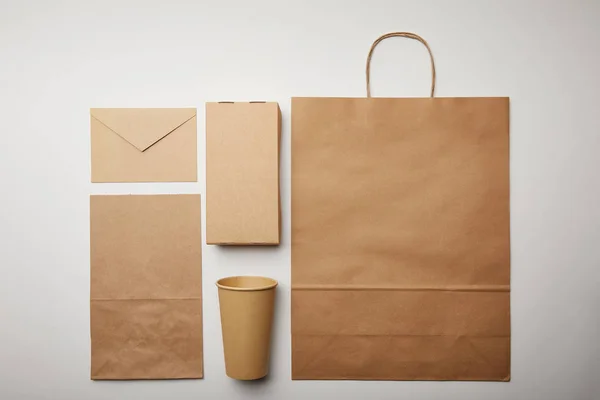 Flay lay with envelope, paper cup, food delivery paper bag on white surface, minimalistic concept — Stock Photo