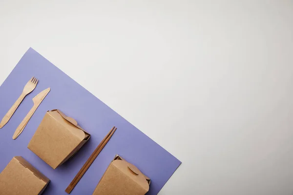 Vista elevada de cajas de fideos, palillos y tenedor desechable con cuchillo en púrpura - foto de stock