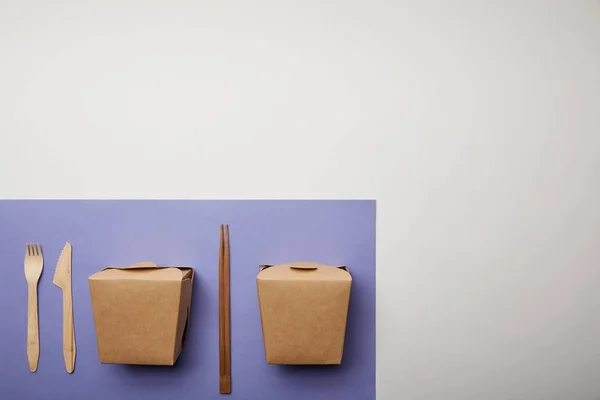 Top view of noodle boxes, chopsticks and disposable fork with knife on purple — Stock Photo