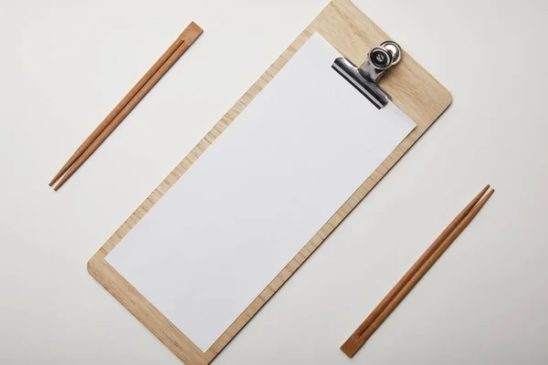 Vue surélevée du menu vierge arrangé et des baguettes sur surface blanche, concept minimaliste — Photo de stock