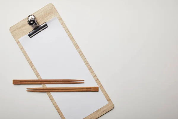 Elevated view of blank menu and chopsticks on white surface, minimalistic concept — Stock Photo