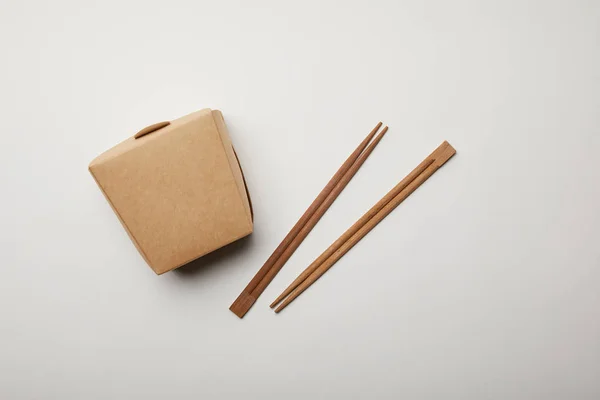 Vista superior de palillos dispuestos y caja de fideos en la superficie blanca, concepto minimalista - foto de stock