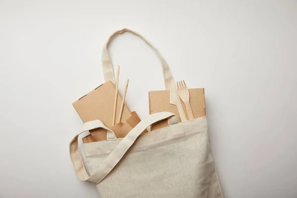 Vista superior de la bolsa de algodón con cajas de alimentos, palillos y tenedores desechables con cuchillos en la superficie blanca - foto de stock