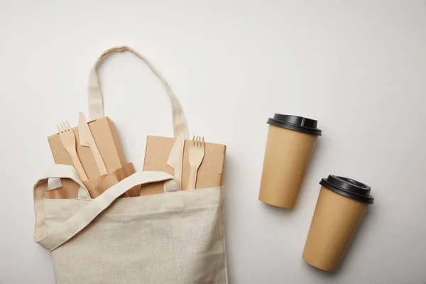 Vista elevada de saco de algodão com caixas de alimentos e duas xícaras de café descartáveis na superfície branca — Fotografia de Stock