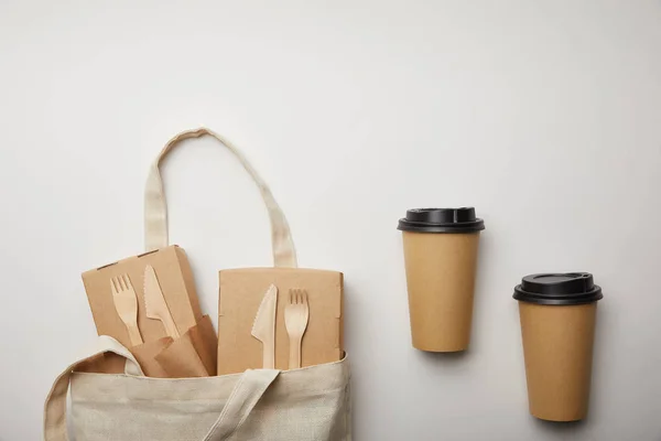 Vue de dessus du sac en coton avec des boîtes à nourriture et deux tasses à café jetables sur la surface blanche — Photo de stock