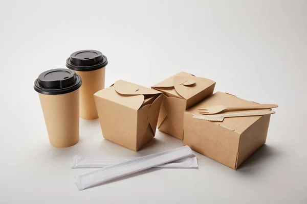 Tenedor desechable con cuchillo, palillos, tazas de café de papel y cajas de cartón sobre blanco - foto de stock