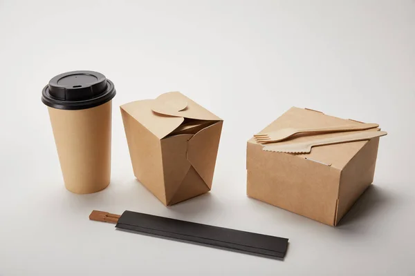 Fourchette jetable avec couteau, tasse à café en papier, boîtes à nourriture et baguettes sur blanc — Photo de stock