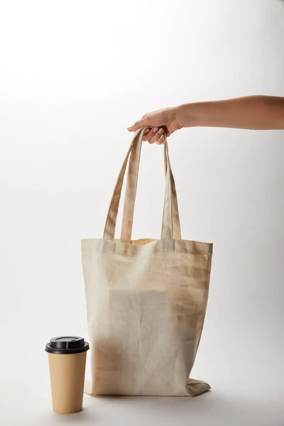Teilansicht der Frau mit Baumwolltasche mit Essensausgabe und Papiertasse Kaffee in der Nähe auf weiß — Stockfoto