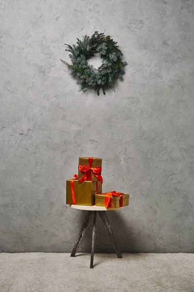 Coffrets cadeaux de Noël dorés avec rubans rouges sur chaise sous couronne de sapin dans la chambre — Photo de stock