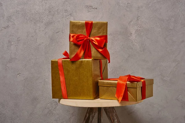 Golden Christmas gift boxes with red ribbons on chair near grey wall in room — Stock Photo