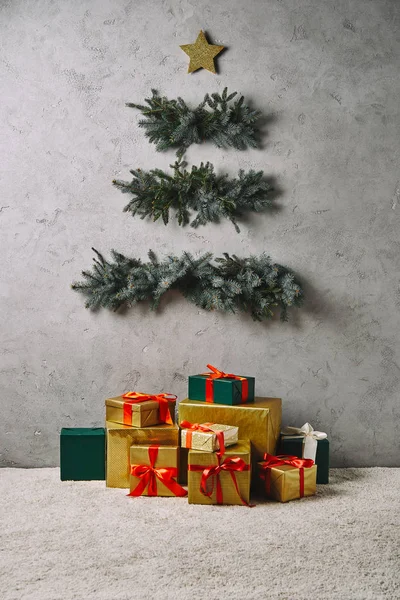 Handmade Christmas tree hanging on grey wall, gift boxes on carpet in room — Stock Photo