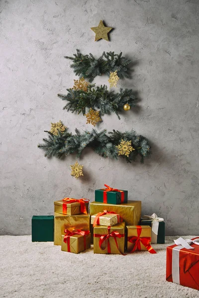 Handcrafted Christmas tree hanging on grey wall, gift boxes on floor in room — Stock Photo
